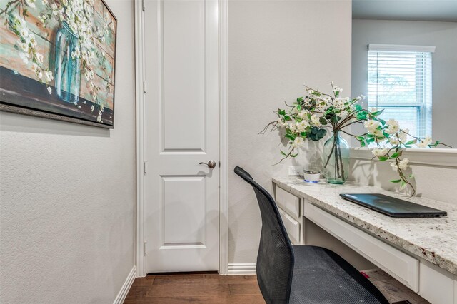 office area featuring built in desk, dark wood-style floors, a textured wall, and baseboards