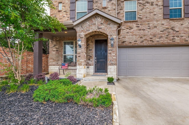 doorway to property featuring an attached garage, concrete driveway, brick siding, and stone siding
