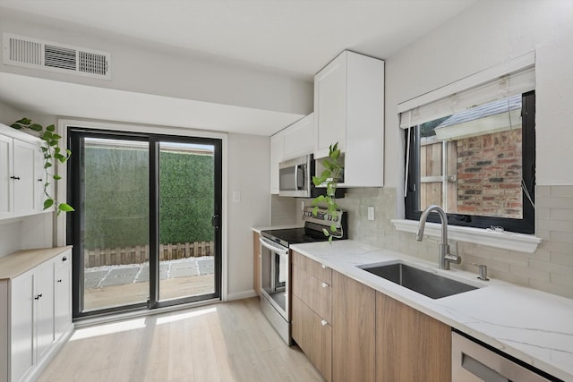 2755 Harbinger Ln, Dallas, TX 75287 - kitchen featuring appliances with stainless steel finishes, a sink, light stone counters, light wood-style flooring, and tasteful backsplash