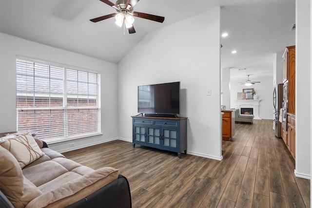 10149 Red Bluff Ln, Fort Worth, TX 76177 - living room featuring ceiling fan, vaulted ceiling, dark wood-type flooring, a lit fireplace, and plenty of natural light