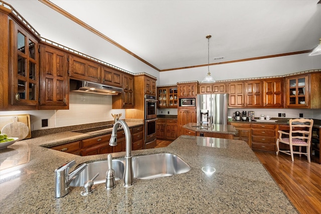 kitchen featuring appliances with stainless steel finishes, under cabinet range hood, a sink, brown cabinets, and crown molding