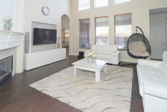 living room featuring a glass covered fireplace, wood finished floors, a towering ceiling, baseboards, and arched walkways