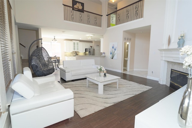 living room featuring wood finished floors, baseboards, a tiled fireplace, and a towering ceiling