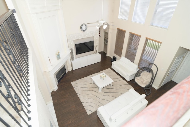 living room featuring a glass covered fireplace, wood finished floors, a ceiling fan, a high ceiling, and baseboards
