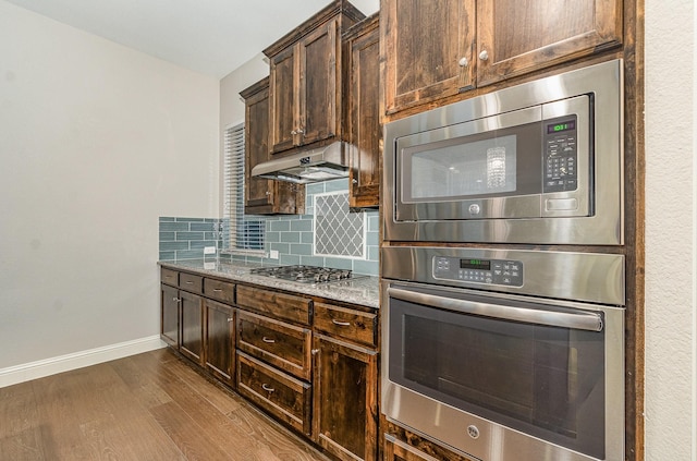413 Allbright Rd, Celina, TX 75009 - kitchen with appliances with stainless steel finishes, under cabinet range hood, light stone counters, baseboards, and dark wood finished floors