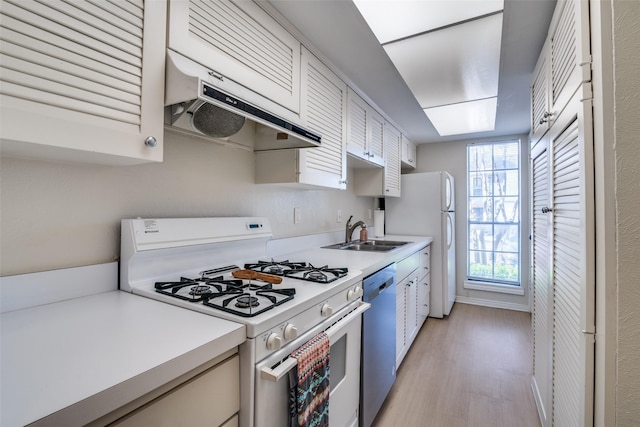 kitchen with white appliances, under cabinet range hood, a sink, and light countertops