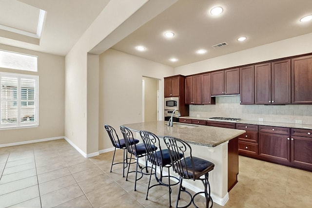 11908 Glenbrook St, Denton, TX 76207 - kitchen with gas stovetop, stainless steel microwave, a sink, a kitchen breakfast bar, and backsplash