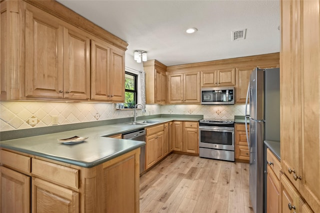 kitchen featuring appliances with stainless steel finishes, a sink, light wood-style flooring, decorative backsplash, and a peninsula