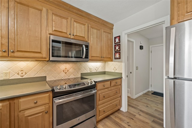 kitchen featuring appliances with stainless steel finishes, light wood finished floors, tasteful backsplash, and baseboards