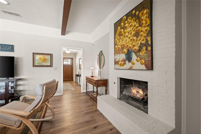 living area featuring beamed ceiling, hardwood / wood-style flooring, a brick fireplace, baseboards, and recessed lighting