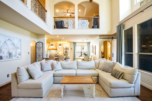 living area with arched walkways, a ceiling fan, a towering ceiling, baseboards, and plenty of natural light