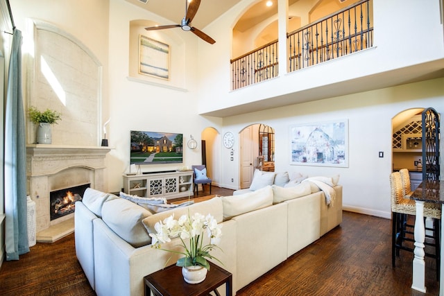 living area featuring a premium fireplace, a ceiling fan, baseboards, wood finished floors, and arched walkways