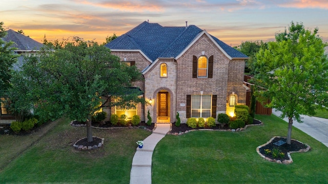 french country inspired facade featuring brick siding, a yard, and roof with shingles