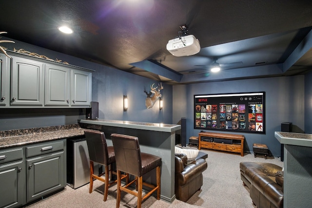 home theater with light colored carpet, a ceiling fan, and a raised ceiling