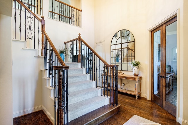 staircase with wood finished floors, baseboards, and a towering ceiling