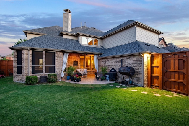 back of house at dusk with roof with shingles, a patio, and brick siding