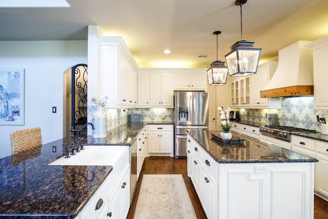kitchen with stainless steel appliances, premium range hood, a peninsula, arched walkways, and dark wood-style flooring