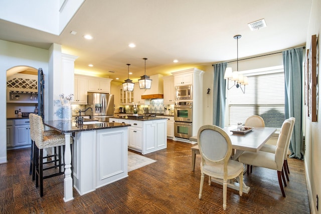 kitchen with stainless steel appliances, a kitchen island, a sink, tasteful backsplash, and dark wood-style flooring