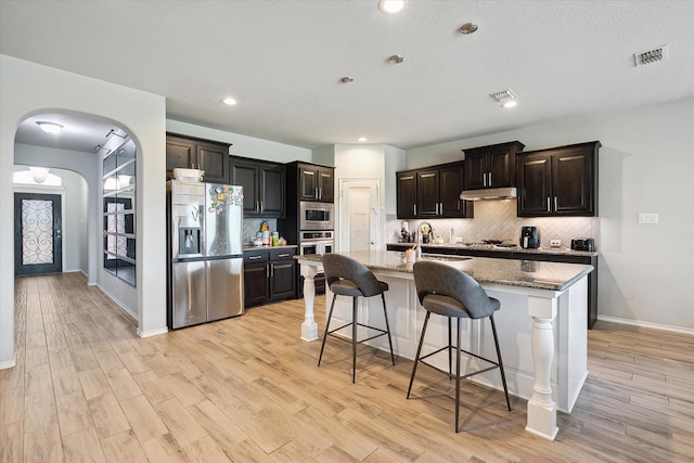 1127 Donnington Trl, Saginaw, TX 76131 - kitchen with stainless steel appliances, under cabinet range hood, arched walkways, decorative backsplash, and a breakfast bar