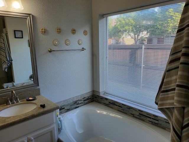 full bath with a bath, vanity, and a textured wall