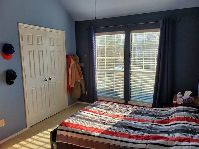 bedroom featuring lofted ceiling, a closet, baseboards, and light colored carpet