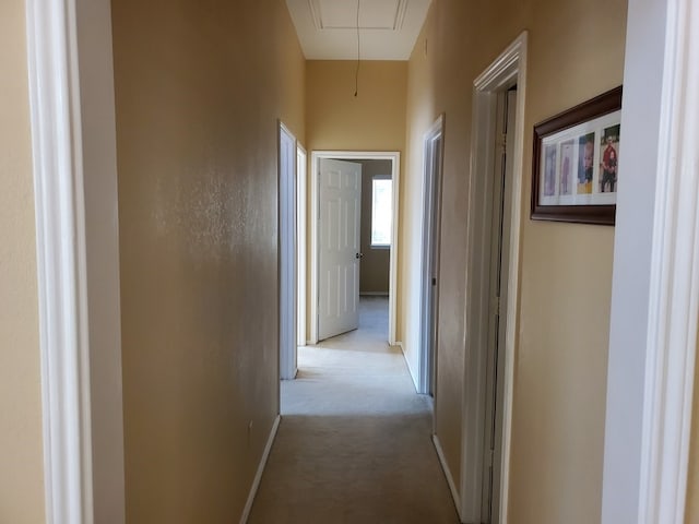 corridor featuring attic access, light carpet, and baseboards