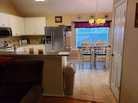 kitchen with appliances with stainless steel finishes, a chandelier, white cabinetry, hanging light fixtures, and vaulted ceiling