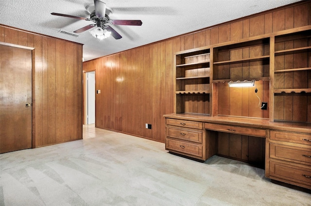 unfurnished office featuring built in study area, wooden walls, light carpet, ceiling fan, and a textured ceiling