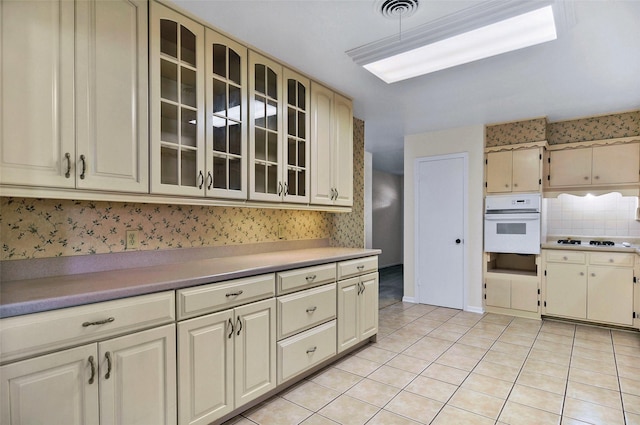 kitchen featuring white appliances, cream cabinetry, light tile patterned flooring, glass insert cabinets, and light countertops