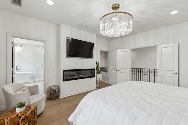 2576 Fountain Cv, Carrollton, TX 75006 - bedroom featuring a chandelier, wood finished floors, a glass covered fireplace, baseboards, and ensuite bathroom