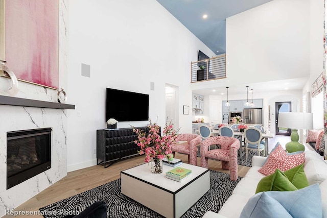 living area featuring light wood finished floors, a high ceiling, a premium fireplace, recessed lighting, and baseboards
