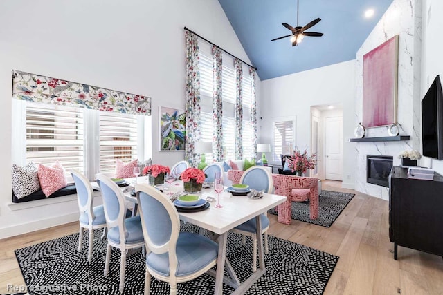 dining room with high vaulted ceiling, a ceiling fan, a premium fireplace, and light wood-type flooring