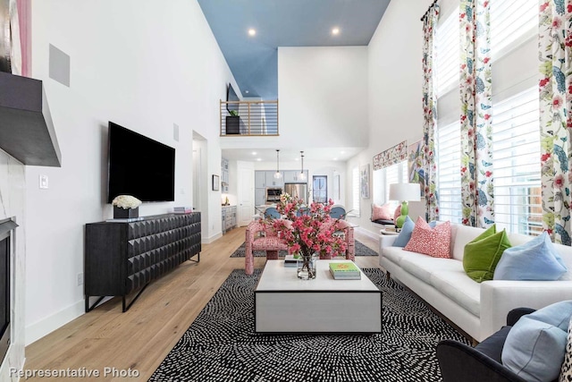 living room featuring a towering ceiling, light wood-style floors, baseboards, and recessed lighting