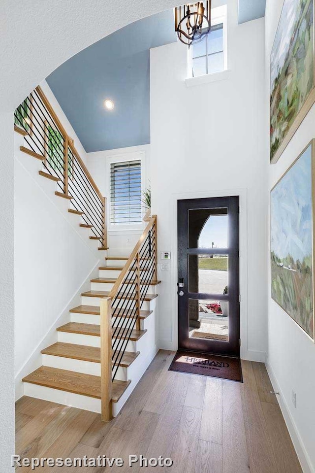 entryway with wood finished floors, stairway, a chandelier, healthy amount of natural light, and a high ceiling
