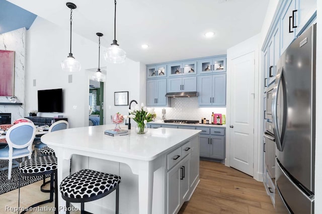 kitchen with stainless steel appliances, under cabinet range hood, a kitchen bar, wood finished floors, and light countertops