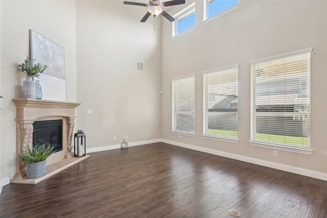 unfurnished living room featuring a ceiling fan, dark wood-style flooring, baseboards, a high ceiling, and a premium fireplace