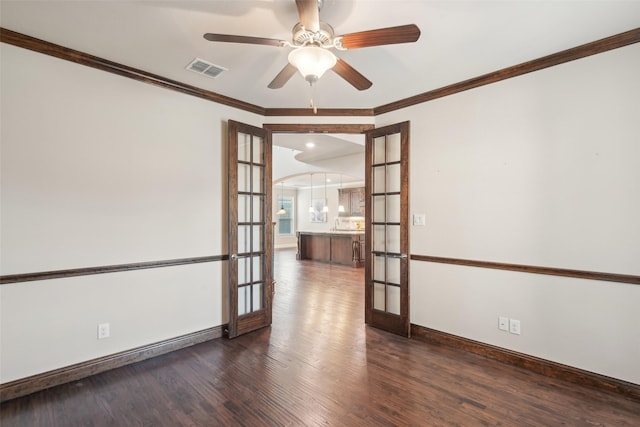 unfurnished room featuring french doors, dark wood-style flooring, baseboards, crown molding, and arched walkways