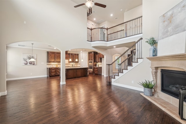 unfurnished living room featuring arched walkways, a ceiling fan, a fireplace, a high ceiling, and baseboards