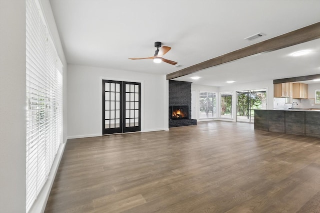 4512 Starlight Dr, Haltom City, TX 76117 - unfurnished living room featuring ceiling fan, dark wood-style flooring, beam ceiling, a brick fireplace, and french doors