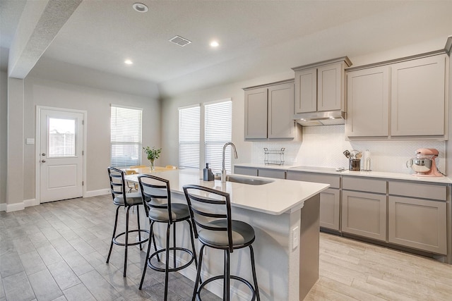 kitchen with gray cabinets, a sink, under cabinet range hood, a center island with sink, and recessed lighting