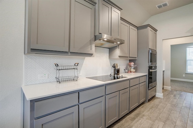 kitchen with gray cabinets, black electric stovetop, wall oven, under cabinet range hood, and tasteful backsplash