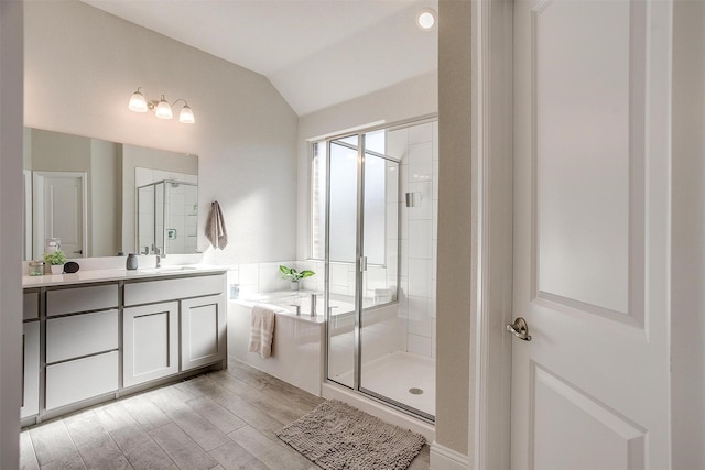bathroom featuring a shower stall, vaulted ceiling, vanity, a garden tub, and wood finished floors