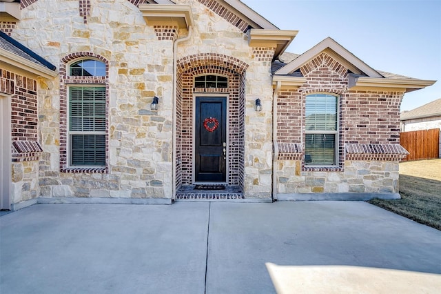 entrance to property with stone siding, a patio area, fence, and brick siding