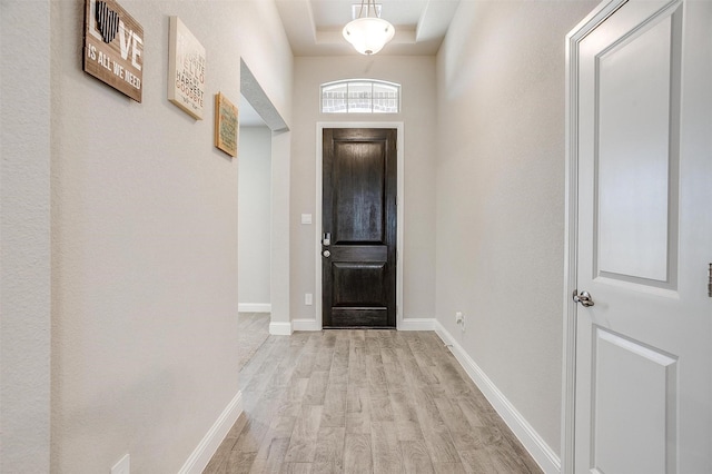 entryway featuring light wood-type flooring, baseboards, and a tray ceiling