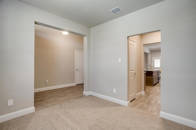 spare room with light colored carpet, baseboards, a sink, and light wood-type flooring
