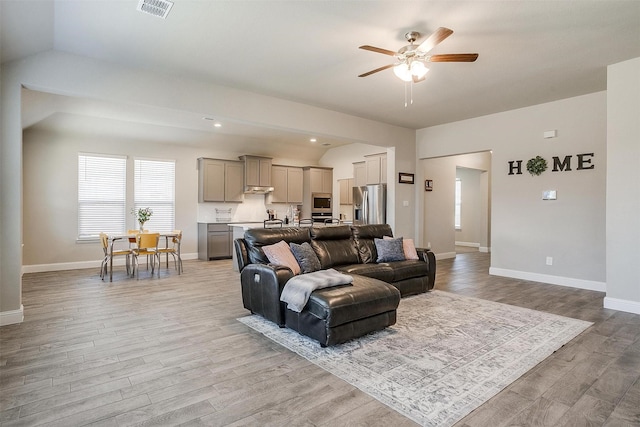 living room featuring a ceiling fan, light wood-style flooring, baseboards, vaulted ceiling, and recessed lighting