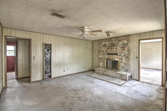43 Pueblo, Gordonville, TX 76245 - unfurnished living room with concrete flooring, a ceiling fan, a stone fireplace, and wooden walls