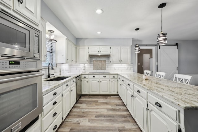 3206 S Fm 51, Decatur, TX 76234 - kitchen featuring a sink, appliances with stainless steel finishes, a peninsula, a barn door, and decorative backsplash