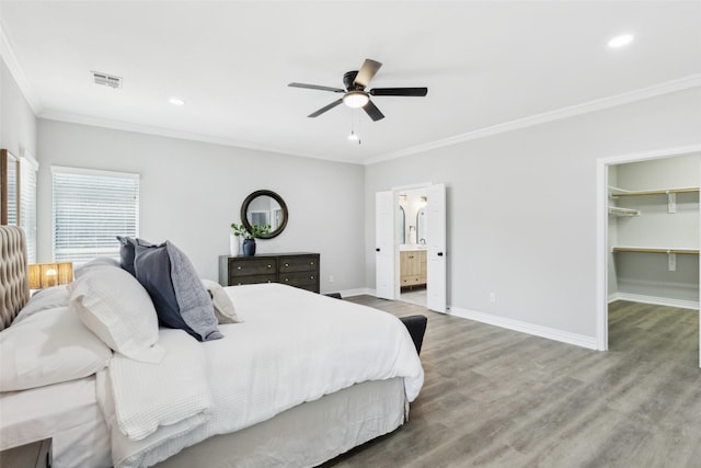 bedroom featuring crown molding, baseboards, wood finished floors, a walk in closet, and recessed lighting
