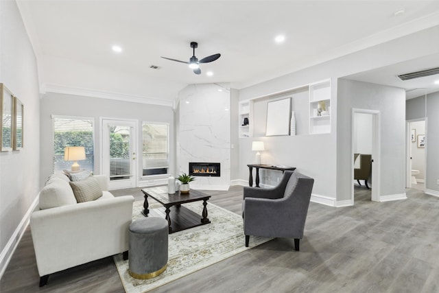living area with ceiling fan, baseboards, a premium fireplace, wood finished floors, and ornamental molding
